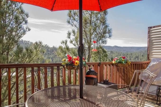 A deck table under a red umbrella looking over the pines and hills