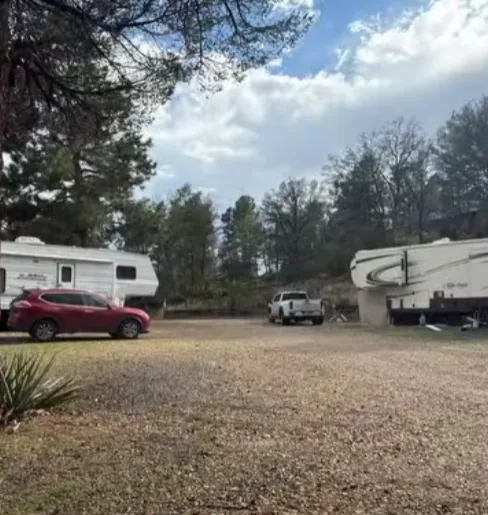 Two fifth wheel RVs and a red SUV on a gravel site