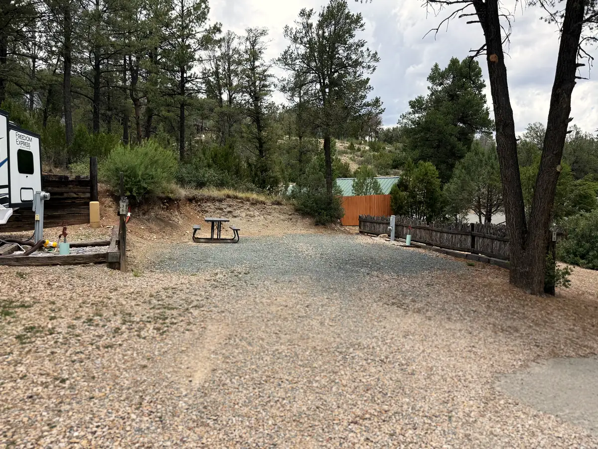 A wide gravel RV site with a picnic table beneath tall Ruidoso pines